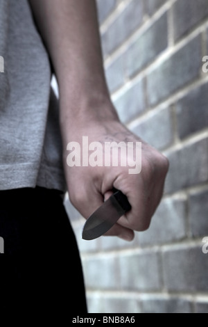 Main d'un jeune homme tenant un couteau en passant devant un mur de briques Banque D'Images