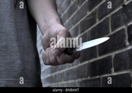 Main d'un jeune homme tenant un couteau en passant devant un mur de briques Banque D'Images