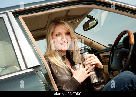 Woman en voiture en stationnement boire le thé thermos Banque D'Images