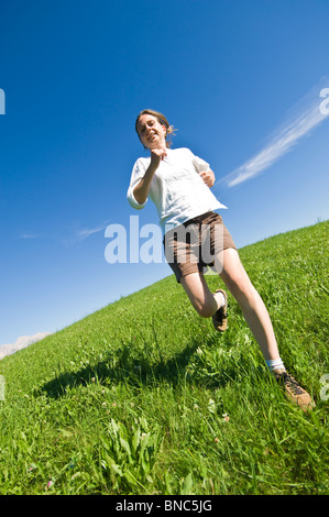 Jeune femme courir et sauter sur une colline herbeuse du Trentin, Italie. Banque D'Images