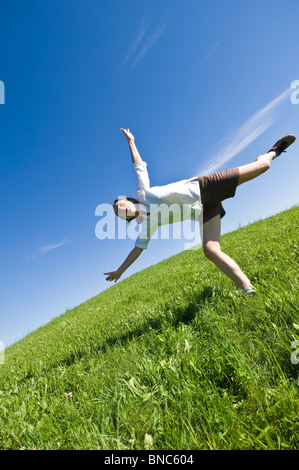 Jeune femme courir et sauter sur une colline herbeuse du Trentin, Italie. Banque D'Images