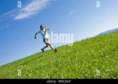 Jeune femme courir et sauter sur une colline herbeuse du Trentin, Italie. Banque D'Images