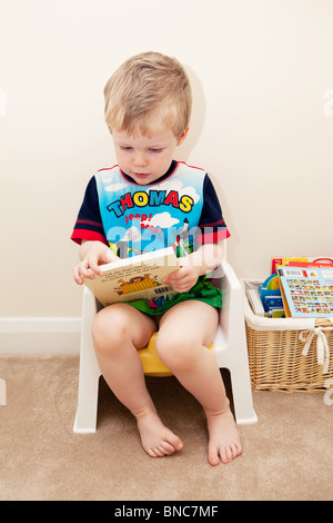 Jeune garçon à la lecture sur son pot. Banque D'Images