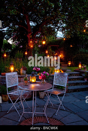 Table et chaises en métal sur patio avec des bougies et des lanternes de jardin la nuit Banque D'Images