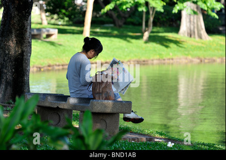 Femme lisant le journal du matin dans la tranquillité au bord du lac dans le parc Lumpini, Bangkok Banque D'Images