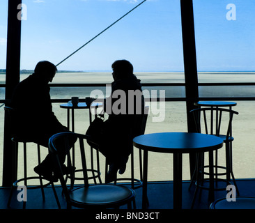 Silhouette d'un couple d'âge moyen assis dans un café en bord de mer sur la jetée de Southport Lancashire England UK avec plage visible derrière Banque D'Images