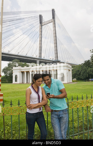 Couple à la recherche d'un téléphone mobile. James Famille Prinsep Memorial, Vidyasagar Setu, Kolkata, West Bengal, India. Bridge en arrière-plan. Banque D'Images