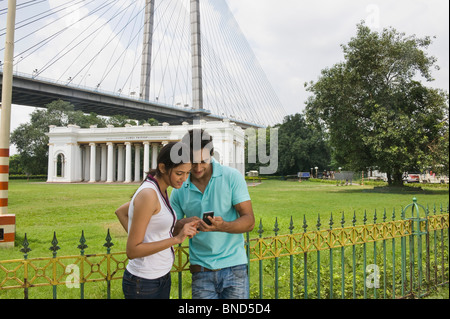 Couple à la recherche d'un téléphone mobile. James Famille Prinsep Memorial, Vidyasagar Setu, Kolkata, West Bengal, India. Bridge en arrière-plan. Banque D'Images