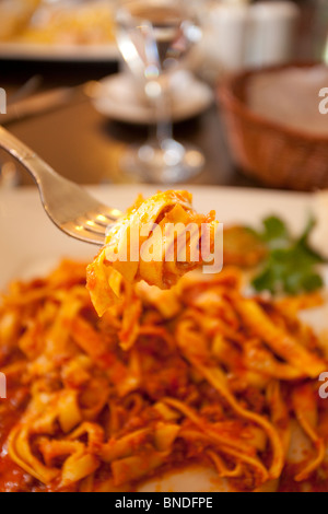 Tagliatelle à la sauce ragu, vue rapprochée de la fourchette avec les pâtes dessus, l'assiette est vue en arrière-plan. Mise au point au premier plan. Banque D'Images