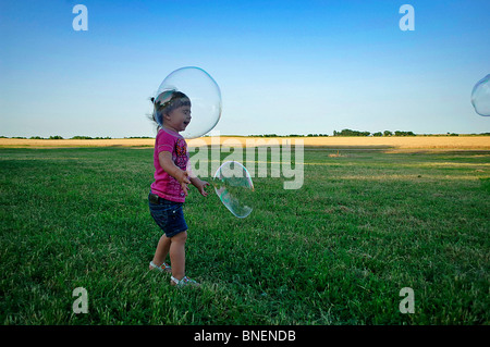 Jeune fille hispanique s'exécute dans l'herbe verte de l'été qu'elle a le pouvoir d'énormes bulles de savon dans la vaste étendue d'un crépuscule à mi-américain Banque D'Images