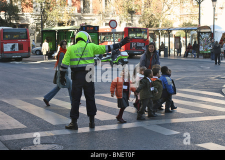 Un "agent de Movilidad' mobilité (agent de police) aide un groupe d'école 8 enfants à traverser la rue Calle de Atocha à Madrid Banque D'Images