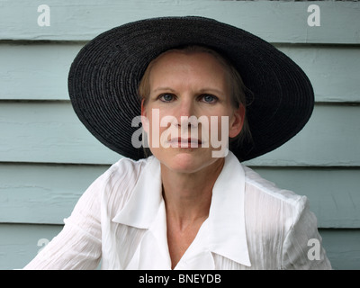 Femme modèle femme en chapeau noir cerclée de large avec chemisier blanc à la caméra directement dans les mains de la mode Banque D'Images