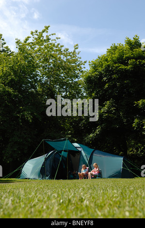 Deux jeunes filles assis dehors un grand green tente familiale baignée de soleil dans un camping avec des arbres derrière Banque D'Images