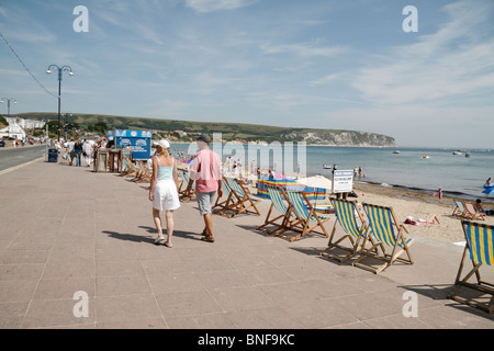 Une ligne passe touristique de transats le long de la promenade de béton au-dessus de la plage de la baie de Swanage, Dorset, UK. Banque D'Images