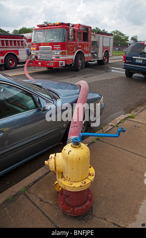 Detroit, Michigan - un tuyau d'incendie est drapé sur une voiture en stationnement illégal à une borne d'incendie Les pompiers bataille l'incendie d'une maison. Banque D'Images