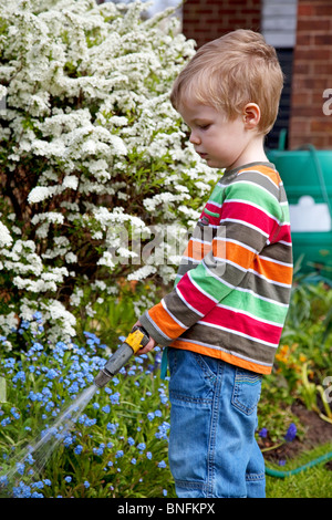 Jeune garçon d'arroser les fleurs dans le jardin. Banque D'Images