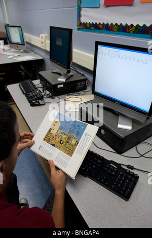 Regarde l'étudiant d'informations sur l'artiste Joan Miro en réserve avant d'utiliser l'ordinateur pour faire des recherches sur internet en ligne sur le sujet Banque D'Images