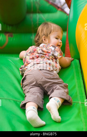 Portrait vertical d'une petite fille ayant beaucoup de plaisir en glissant sur un toboggan gonflable à l'aide d'un aire de jeux. Banque D'Images