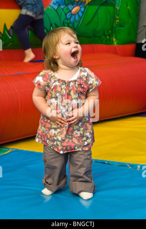 Portrait vertical d'une petite fille ayant beaucoup de plaisir sur un inflatible bouncy castle à une aire de jeux. Banque D'Images