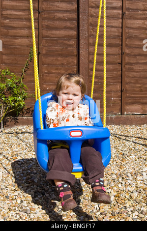 Portrait vertical d'une petite fille ayant beaucoup de plaisir poussés dans une balançoire dans le jardin arrière. Banque D'Images