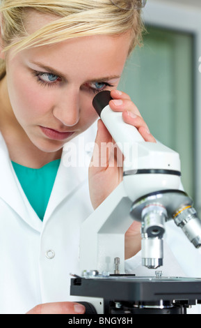 Une belle blonde aux yeux bleus, femme scientifique médicale ou d'une femme libre de son microscope dans un laboratoire. Banque D'Images