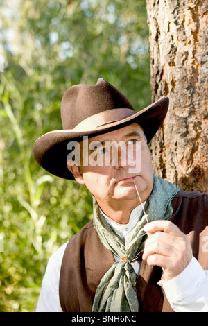 Plus beau cowboy à mâcher sur un peu de foin, appuyé contre un arbre Banque D'Images