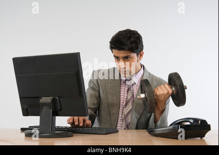 Man exercising with dumbbells et travaillant sur un ordinateur Banque D'Images