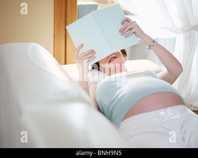 L'italien de 7 mois femme enceinte couchée sur un canapé et la lecture de livre. De forme horizontale, high angle view, Copy space Banque D'Images