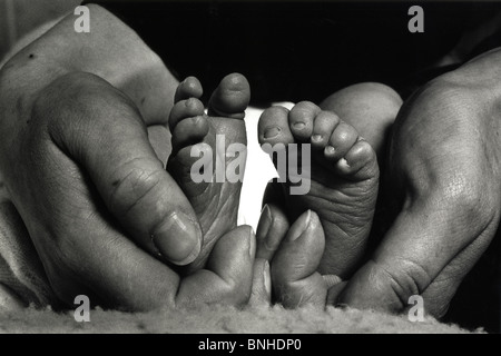 Une nouvelle mère berceaux son nouveau-né bébé petits pieds dans ses mains à Soweto, Johannesburg, Afrique du Sud Banque D'Images