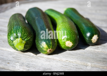 Quatre courgettes ou zucchinis sur une ligne sur une table en bois. Banque D'Images