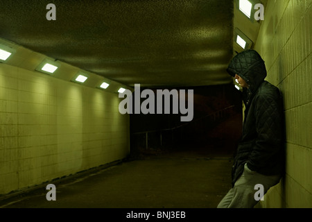 Teenage boy leaning against wall de métro la nuit. Banque D'Images