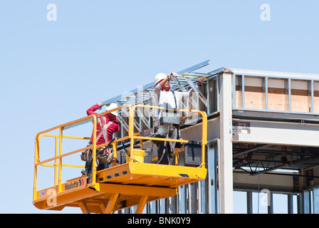 Les travailleurs de la construction sur une plate-forme élévatrice à ciseaux sont l'assemblage de membrures en acier sur un nouveau bâtiment commercial. Banque D'Images