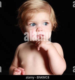 Bébé tête rouge d'oeil sur le côté avec le doigt dans la bouche. Elle a l'air pensif et perplexe. Banque D'Images