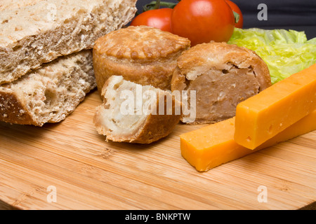 Le déjeuner traditionnel anglais Plowmans de fromage, pain, tomate, laitue et pork pie sur plateau en bois. Banque D'Images