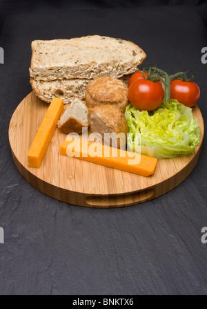 Le déjeuner traditionnel anglais Plowmans de fromage, pain, tomate, laitue et pork pie sur plateau en bois. Banque D'Images