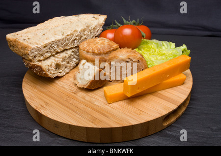 Le déjeuner traditionnel anglais Plowmans de fromage, pain, tomate, laitue et pork pie sur plateau en bois. Banque D'Images