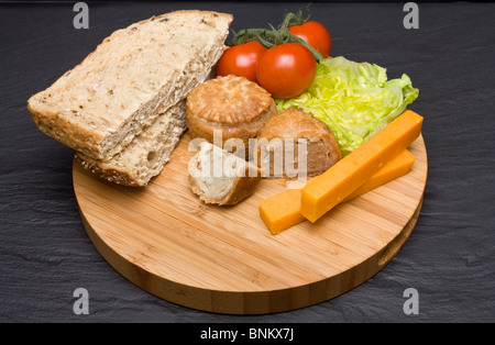 Le déjeuner traditionnel anglais Plowmans de fromage, pain, tomate, laitue et pork pie sur plateau en bois. Banque D'Images