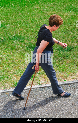 Mature / middle-aged woman walking partiellement handicapée avec stick - France. Banque D'Images
