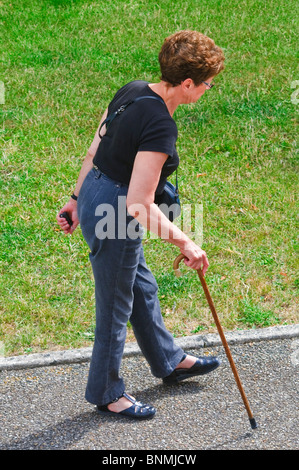 Mature / middle-aged woman walking partiellement handicapée avec stick - France. Banque D'Images