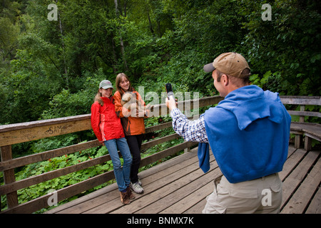 Père utilise un téléphone cellulaire pour prendre une photo de ses deux filles adolescentes tenant un chiot, sur les chutes de Thunderbird, Alaska Banque D'Images