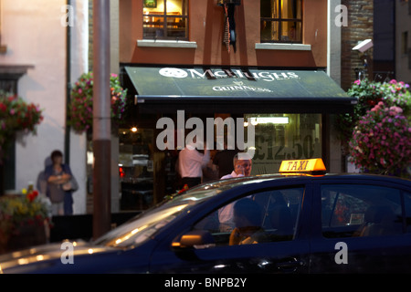 L'homme sur un téléphone mobile est dans un taxi à l'extérieur de nuit pub McHughs dans le centre-ville de Belfast en Irlande du Nord au Royaume-Uni. Banque D'Images