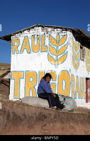 Fille assise sur le rocher à l'extérieur de la maison peinte avec de la propagande pour le candidat du Parti du blé pour les élections locales, près de Yanaoca, région de Cusco, Pérou Banque D'Images