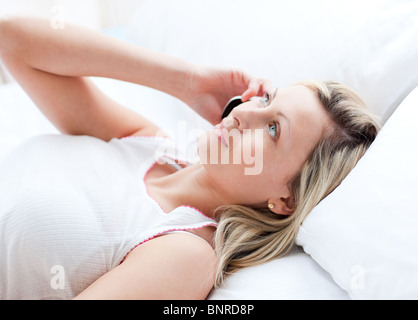 Blonde Woman talking on phone lying on a bed Banque D'Images