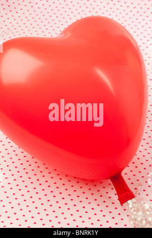 Un ballon en forme de coeur rouge sur un fond de lumière de petits coeurs roses Banque D'Images