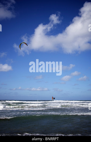 Kitesurfer saute haut sur son kitesurf sur une journée ensoleillée avec quelques nuages dans le ciel. Banque D'Images