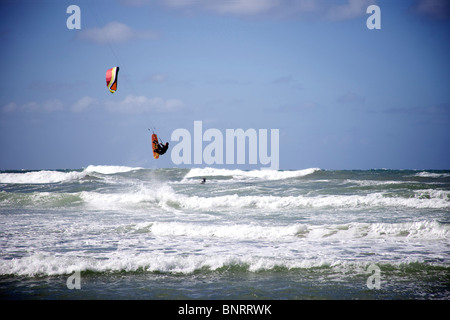 Un homme saute sur son haut kitesurfer kitesurf tandis qu'un autre homme des tours en arrière-plan. Banque D'Images