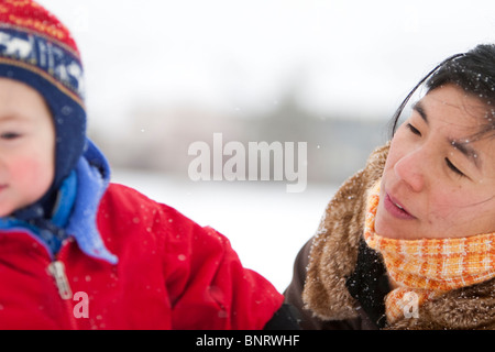 Un garçon de deux ans joue dans un champ neigeux pendant une tempête dans un habit rouge avec sa mère dans un parc, Fort Collins, Colorado Banque D'Images