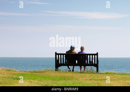 Vue arrière du couple de personnes âgées assis sur banc de falaise face à la mer Banque D'Images