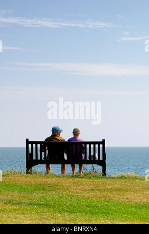 Vue arrière du couple de personnes âgées assis sur banc de falaise face à la mer Banque D'Images