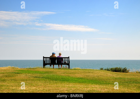 Vue arrière du couple de personnes âgées assis sur banc de falaise face à la mer Banque D'Images